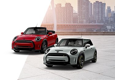 Three-quarter front view of two MINIs, one red and one silver, parked on a stone surface rooftop with a city skyline in the background.