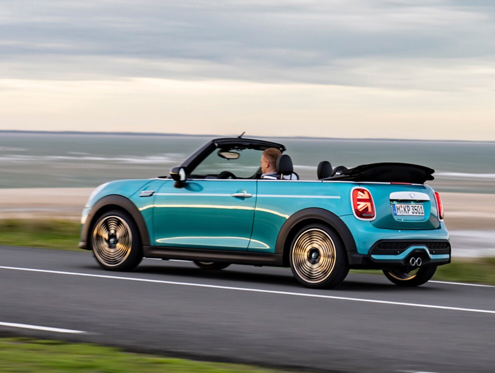 A MINI Cooper Convertible driving along the beach with the top down.